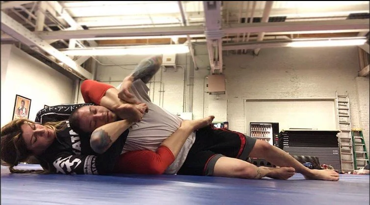 Women's empowerment expert dr. Alice Atalanta in the  mma gym doing jiujitsu bjj with a male partner and putting him in a submission