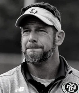 A bearded man, a US Army Ranger named LTC JC Glick, wearing a visor and a sports jacket, looking thoughtful.