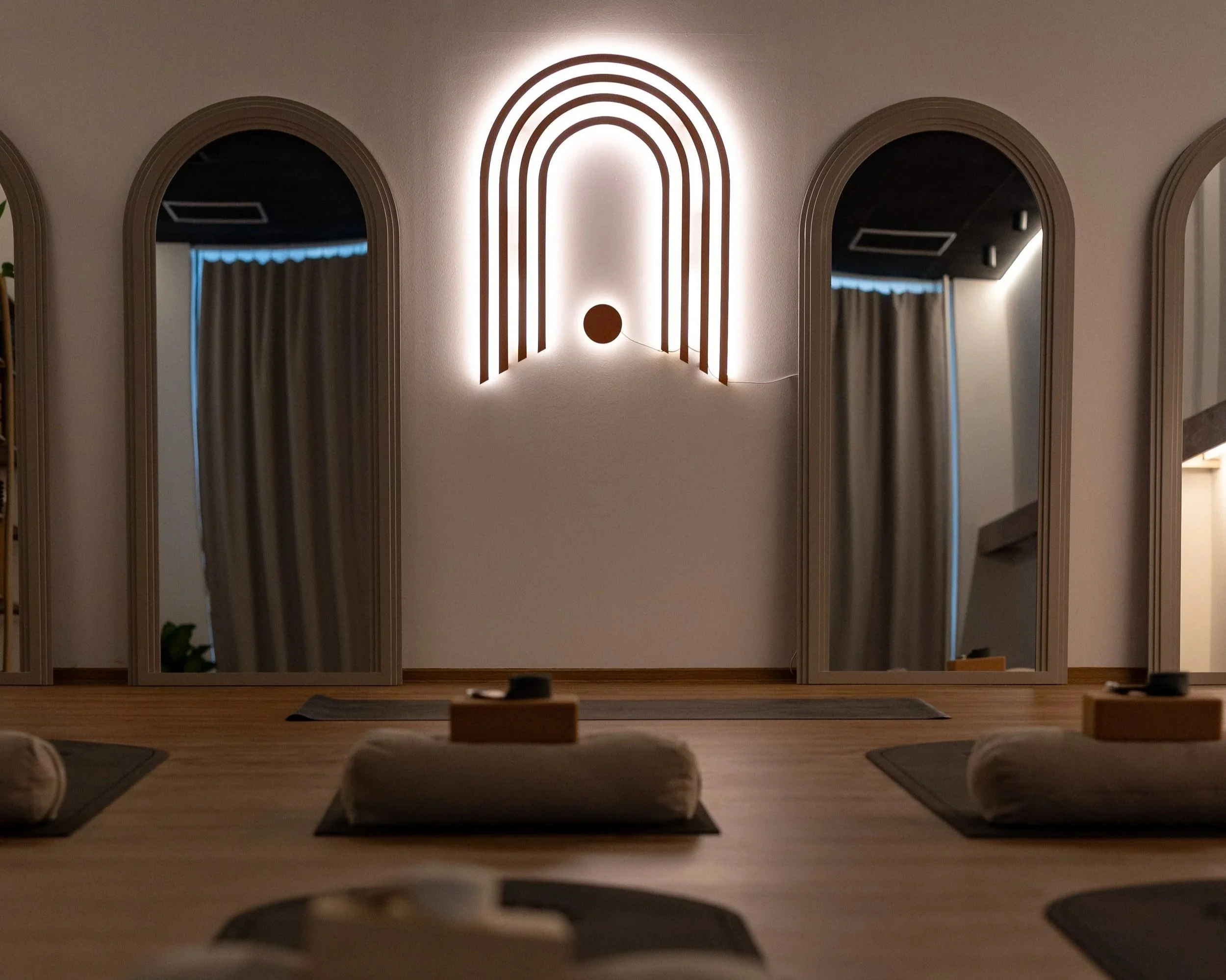 A yoga or meditation room with a wall featuring arched mirrors and a rainbow-shaped wooden wall decor with backlighting.