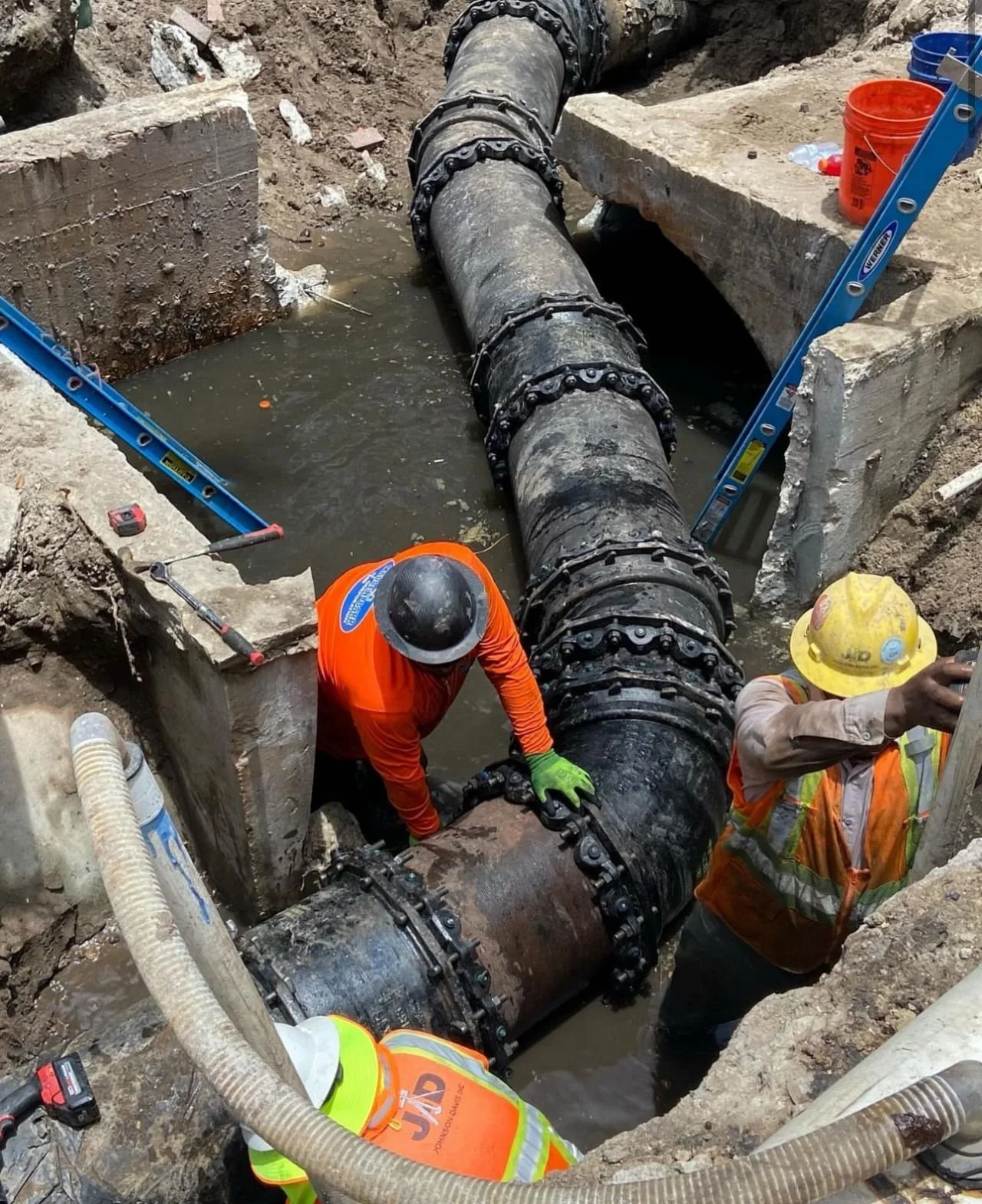 Construction workers in safety gear repairing or installing a large underground pipe at a construction site.