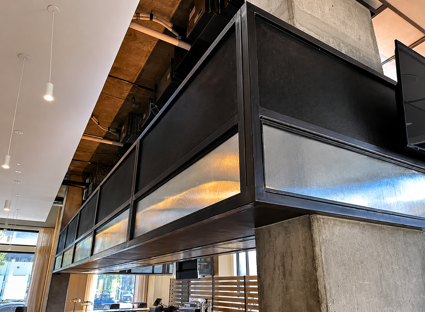 Interior of a modern restaurant or cafe with a concrete pillar, black metal and frosted glass divider, white ceiling with hanging lights, and large windows letting in natural light.
