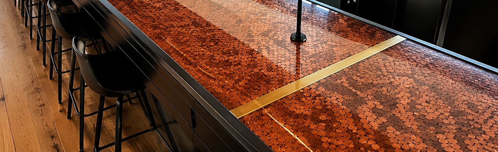 A long bar counter embedded with pennies, with black bar stools on one side and a wooden floor underneath.