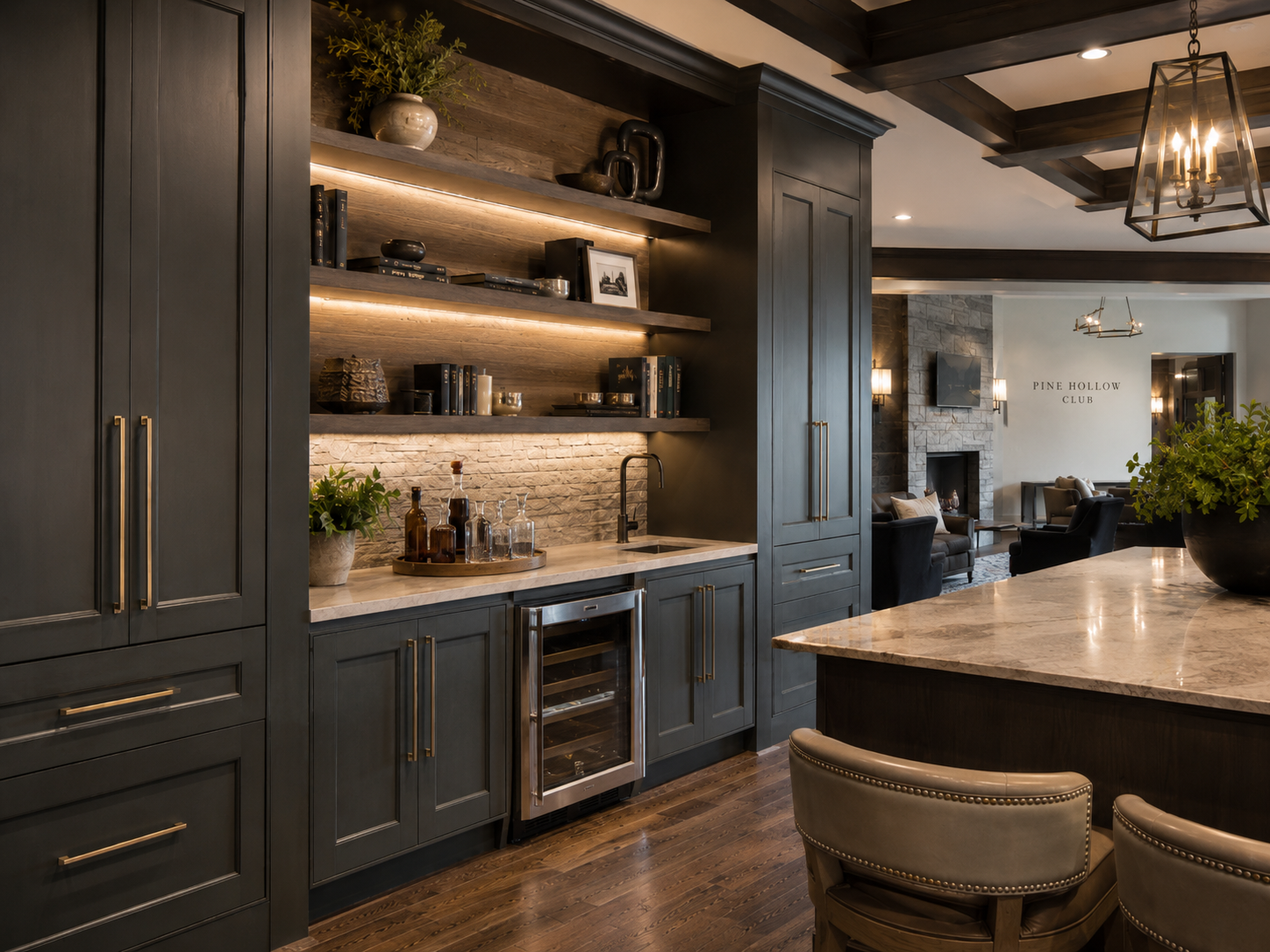 A modern kitchen with dark gray cabinets, open wooden shelves with books and decorative items, a small wine fridge, a marble countertop with bottles and glassware, and a living room area with a fireplace and TV in the background.