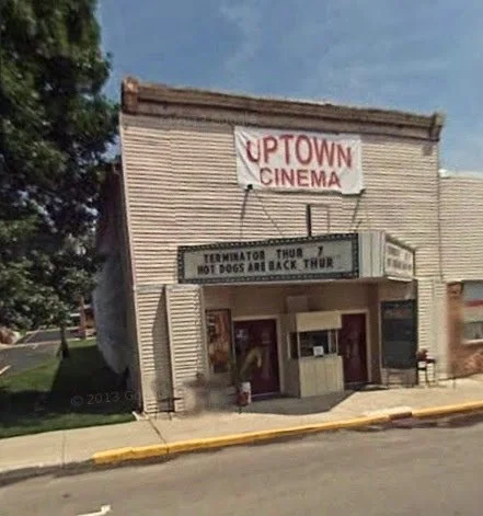 An old building with a sign that reads 'Uptown Cinema' and a marquee advertising 'Terminator Thru 7, no dogs are black throat.'