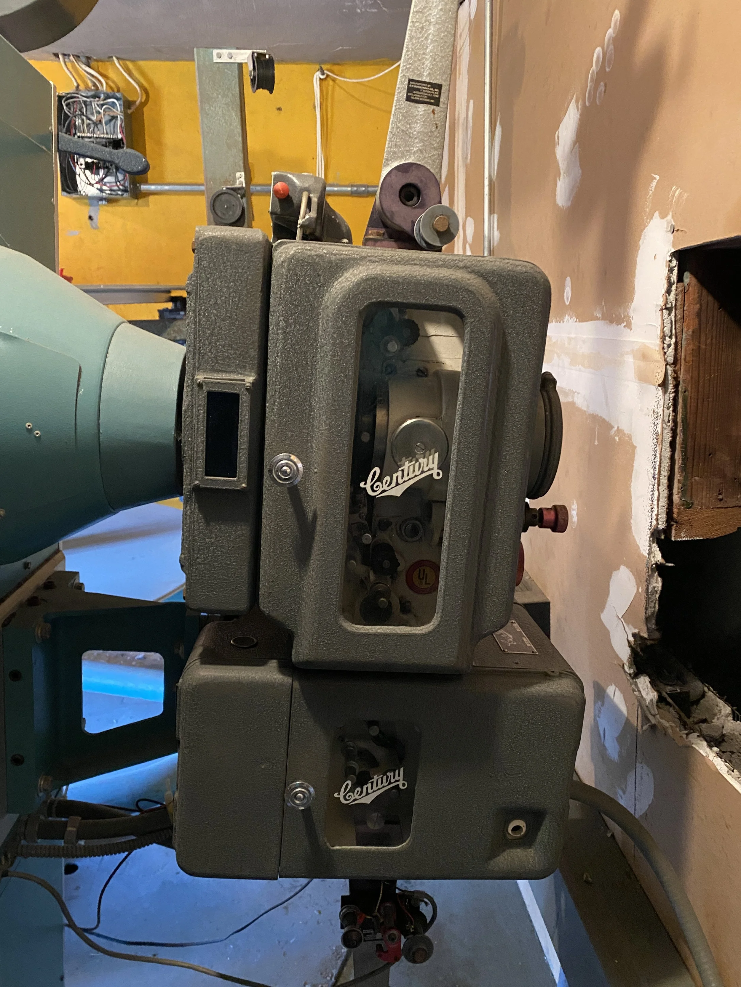 A vintage cinema projector, labeled 'Century,' is positioned in a projector booth.