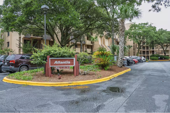 Apartment complex parking lot with a sign for Atlantis, surrounded by greenery and trees, and cars parked along the curb.