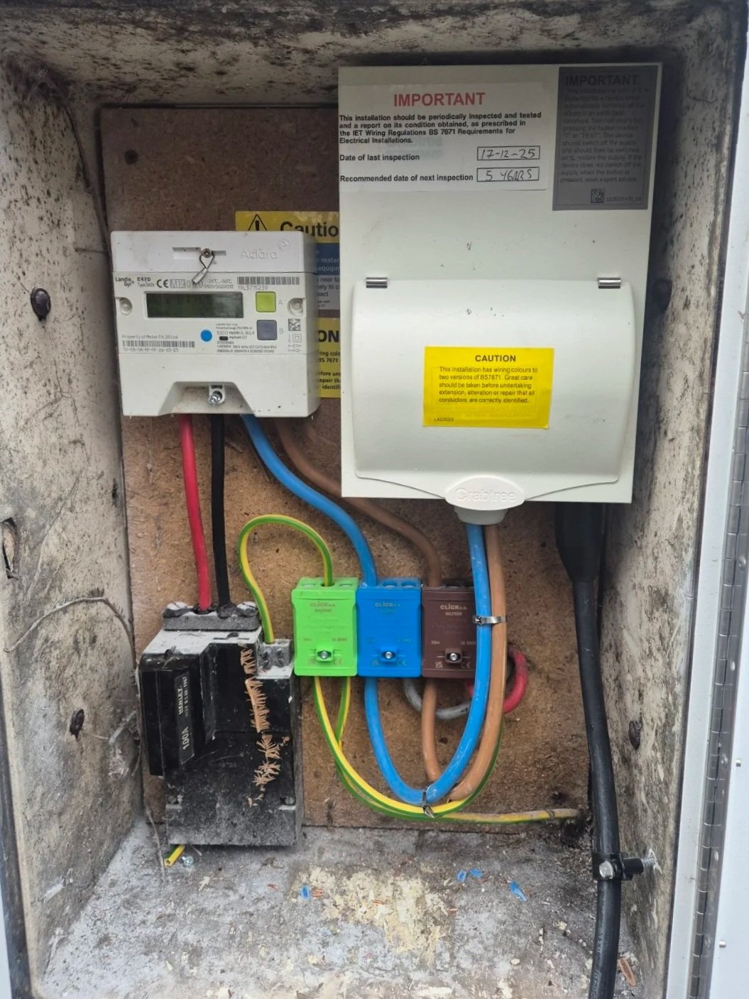 Electrical meter box with wiring components, circuit breakers, and inspection and caution labels inside a metal enclosure.