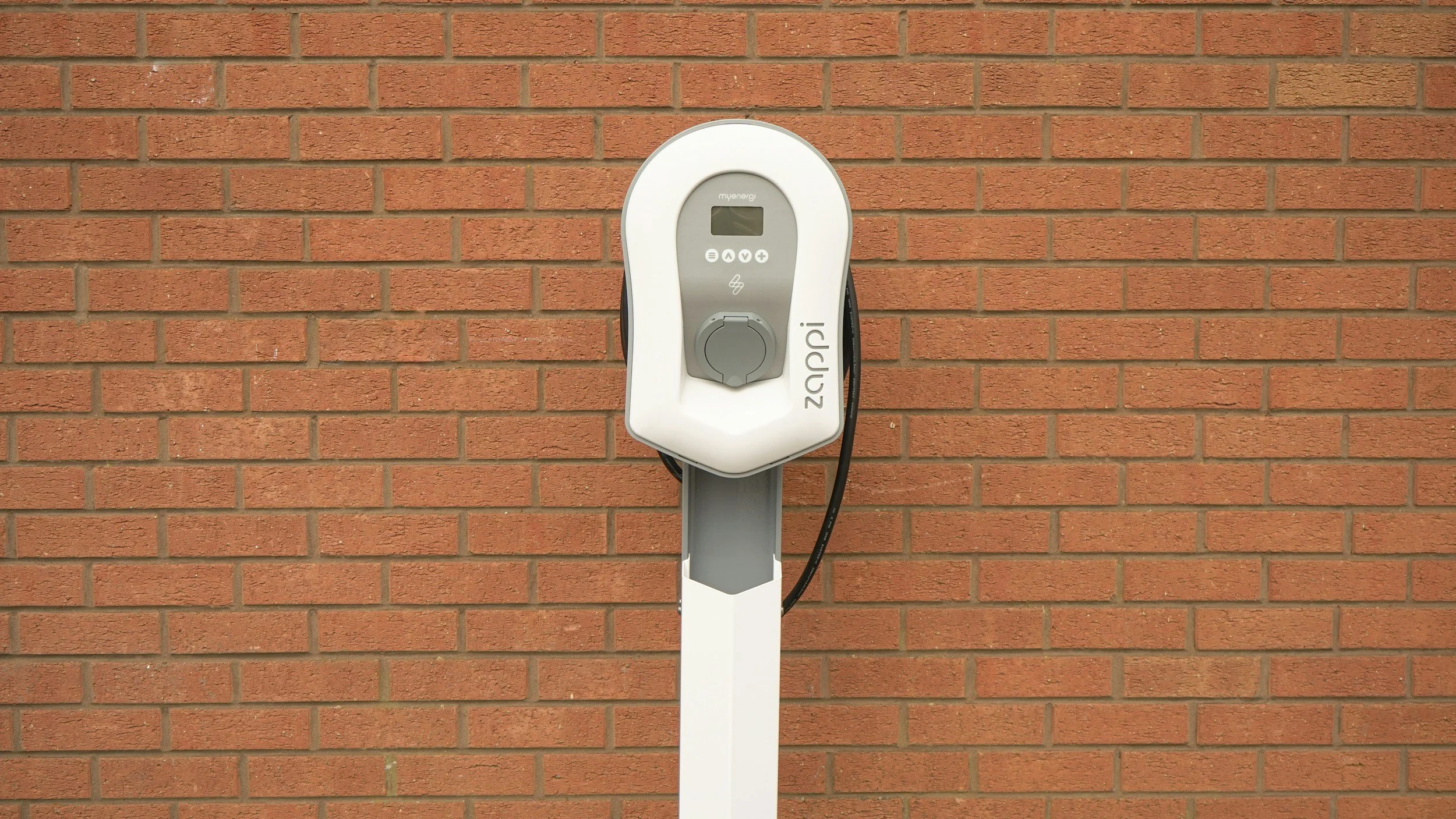 Electric vehicle charging station mounted on a pole in front of a brick wall.