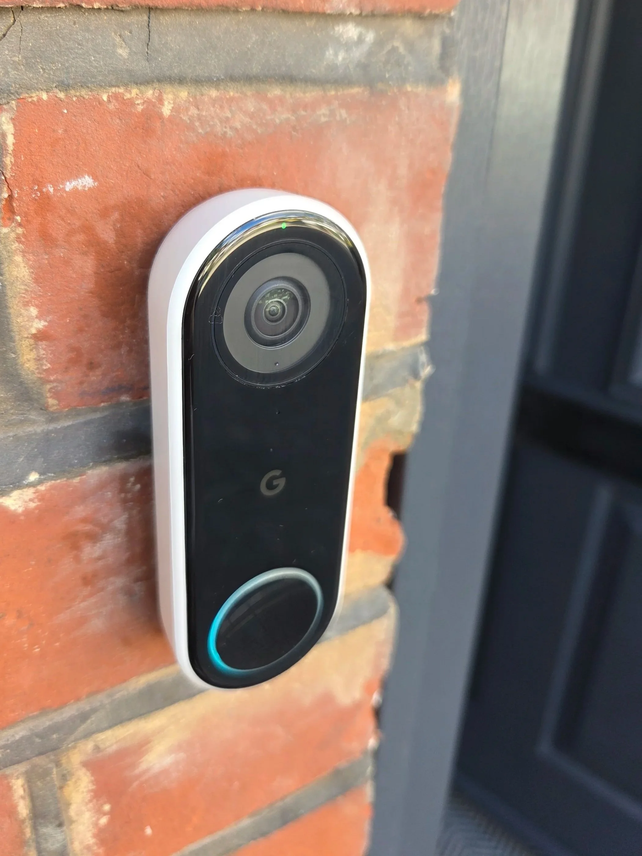 Google Nest Hello video doorbell mounted on a brick wall beside a black door frame in Enfield.