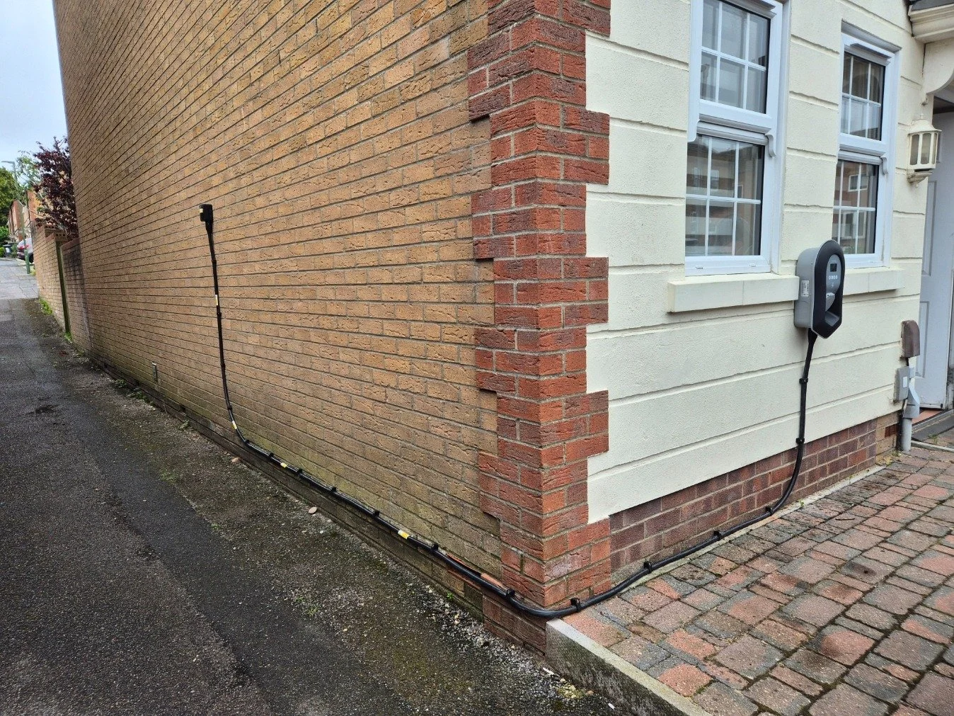 External view of a house showing a color-changed exterior wall with a Zappi EV charging station installed on the wall, with cables running to the ground.