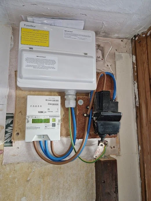 Electrical panel with circuit breaker, connected to a digital energy meter, mounted on a wooden board against a wall.