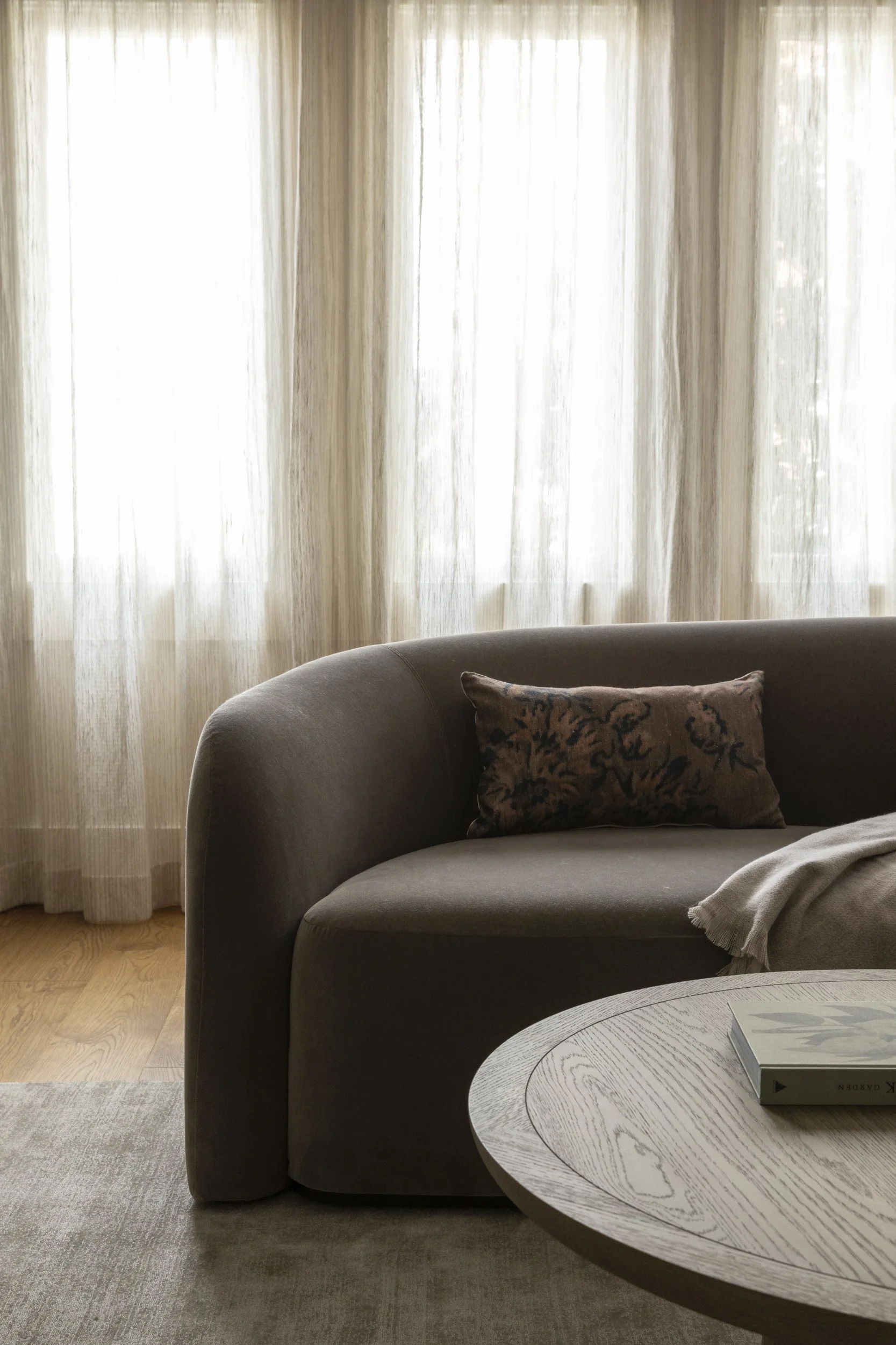 Living room with beige curtains, a gray sofa with decorative pillow, a blanket, and a wooden coffee table with a book on it.