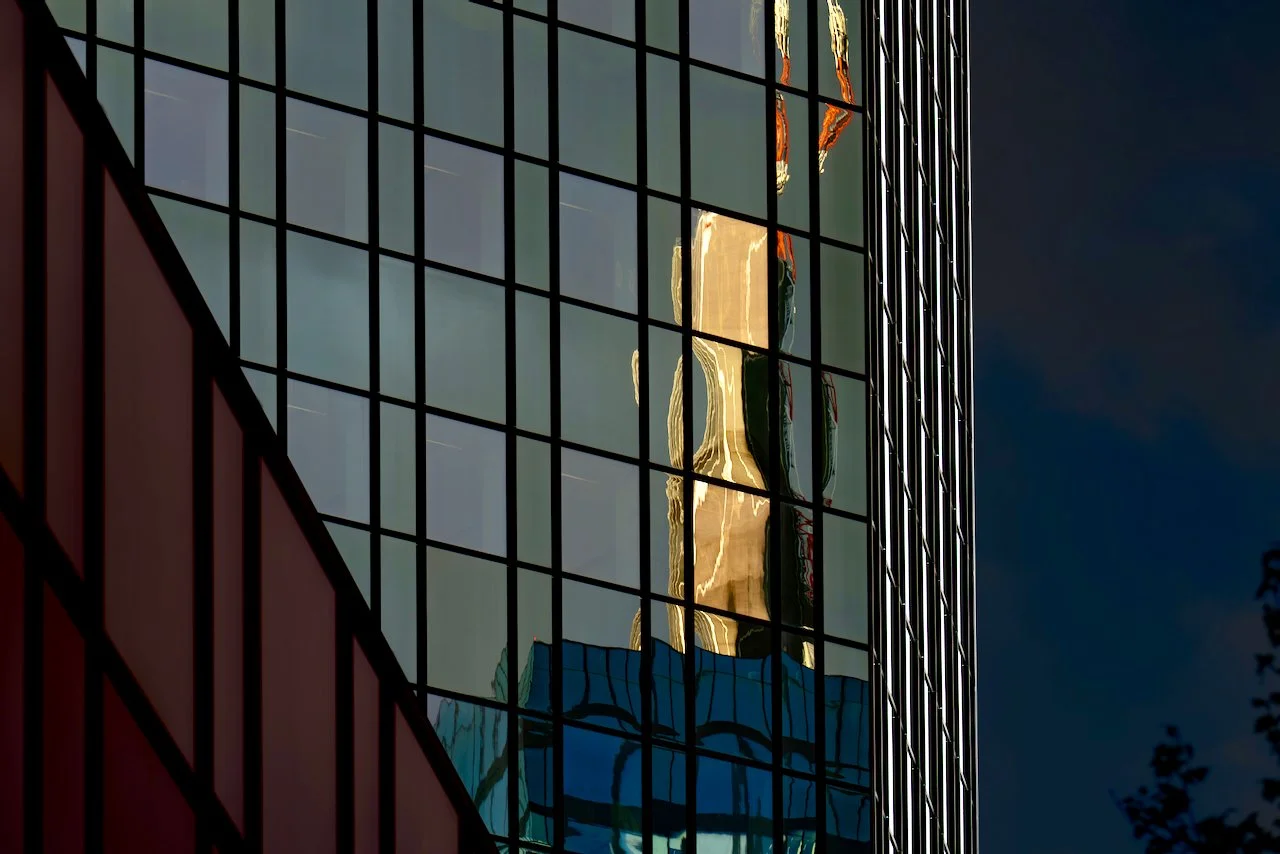 Reflected image of a person on the glass window of a building, with grid-style framing, against a dark sky.
