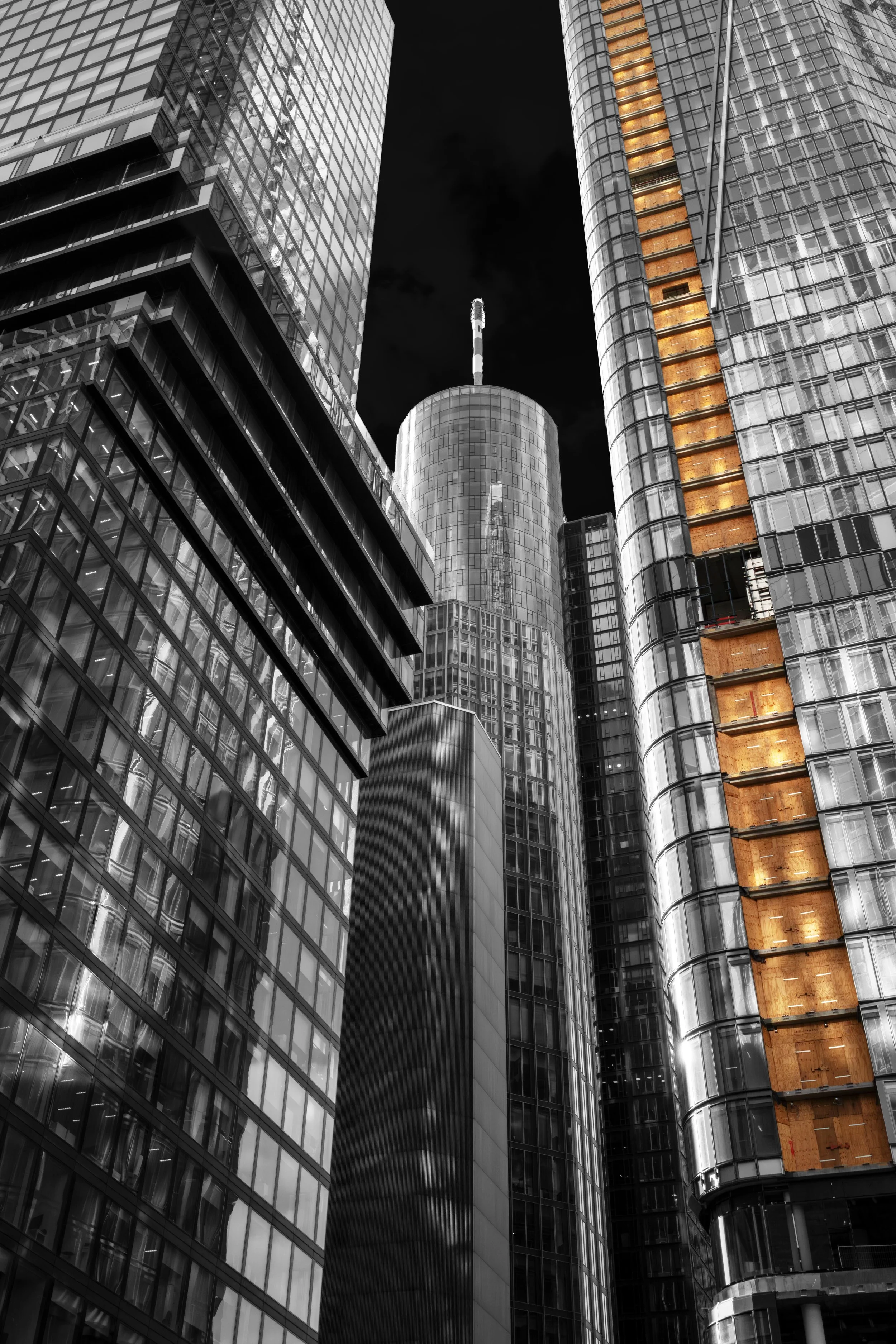 Tall modern glass skyscrapers at night, with one building under construction and illuminated floors visible.