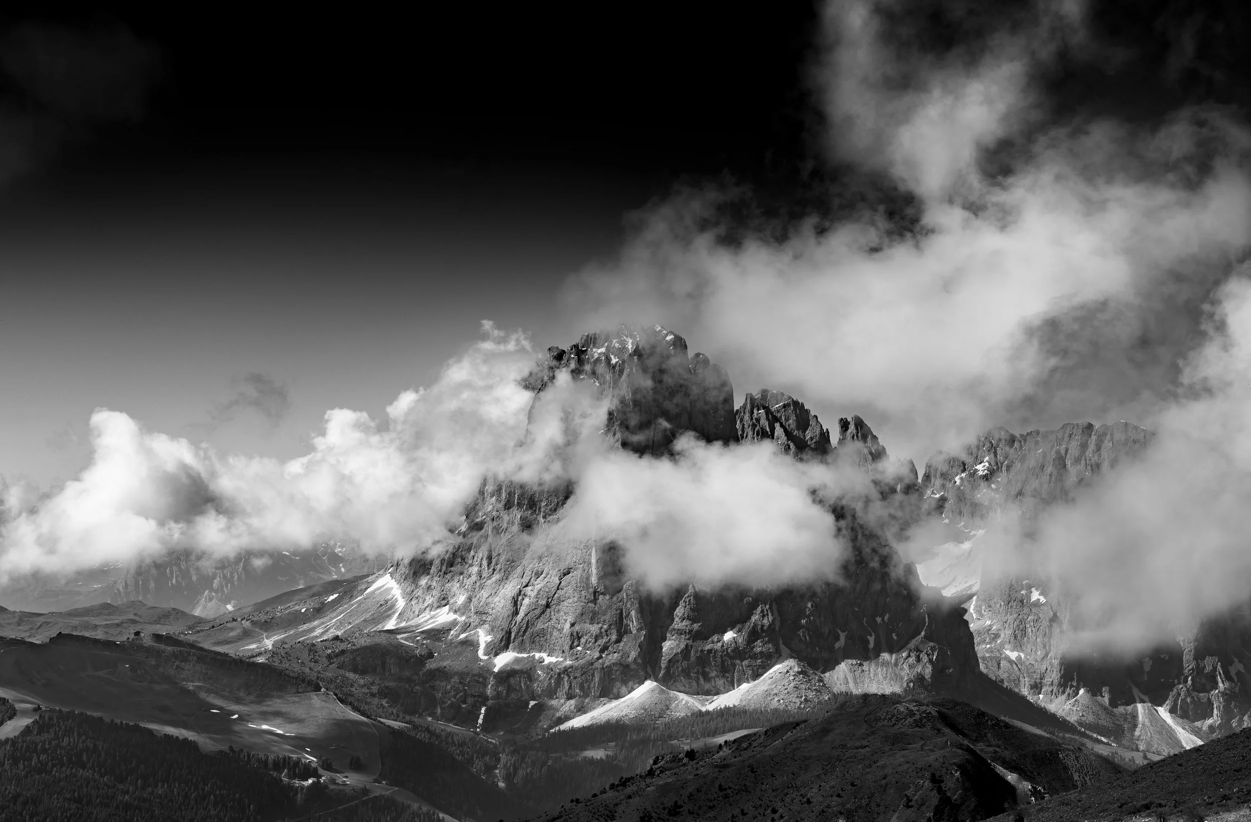 Black and white photo of a mountain peak surrounded by clouds and lower mountain ranges.