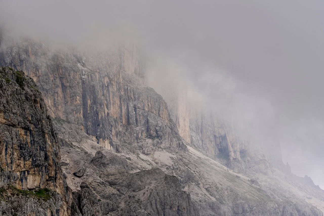 A rugged mountain slope with steep cliffs partially obscured by fog and low-hanging clouds.