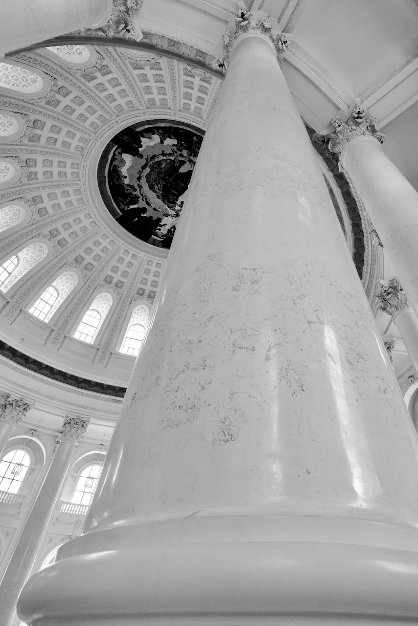 View of a large marble column and ornate ceiling with a mural inside a grand historical building, likely a government or historic building with neoclassical architecture.