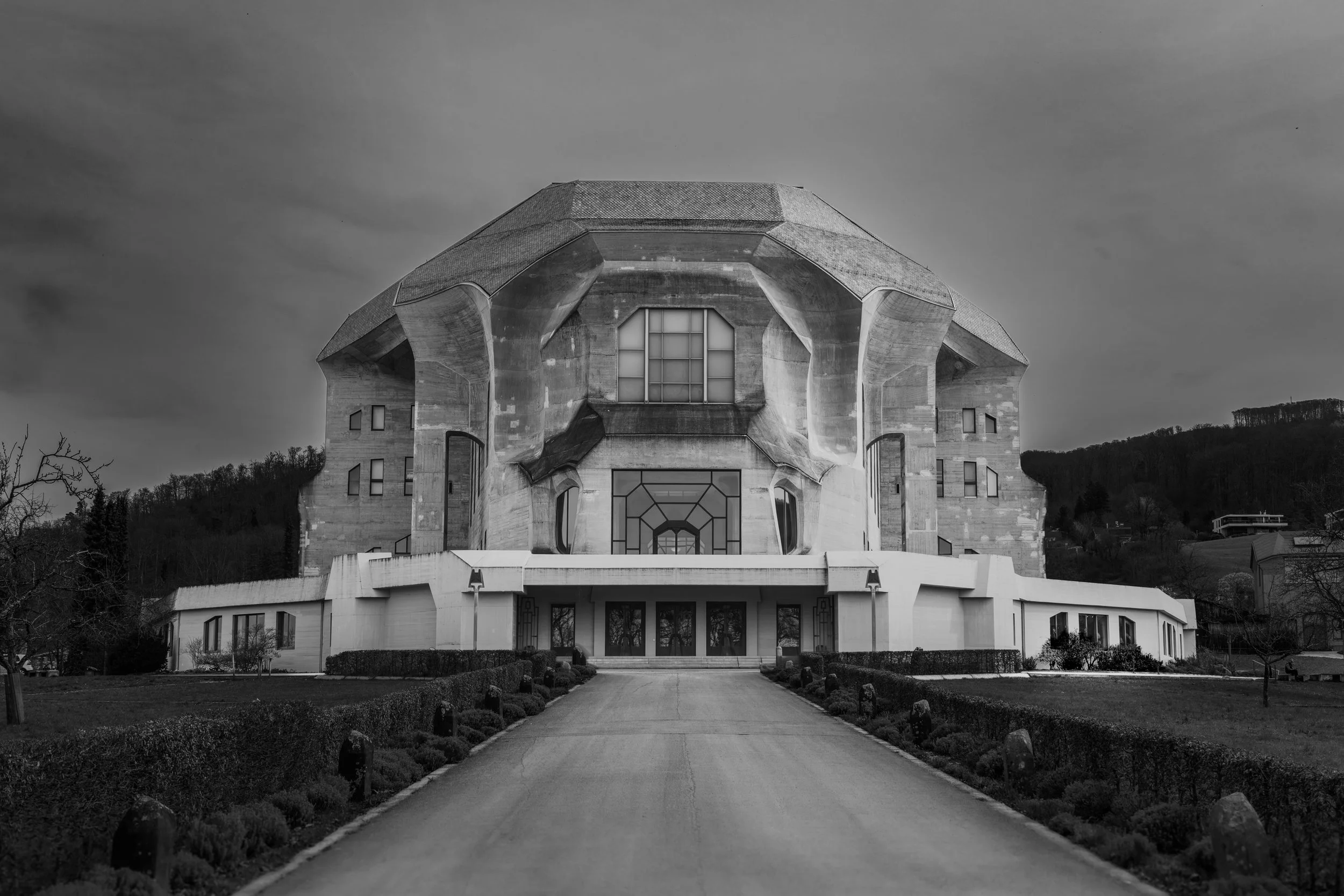 Black and white photo of a modern building with an unusual, sculptural design, set against a cloudy sky and surrounded by manicured landscaping.