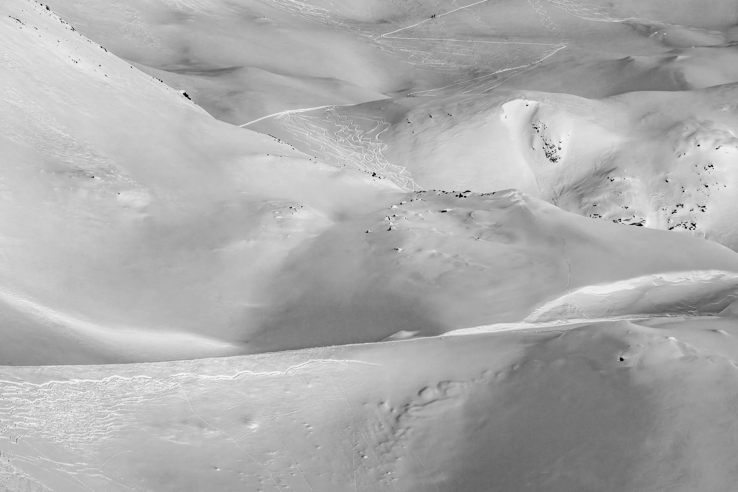 A snowy mountain landscape with ski tracks and a few skiers in the distance.