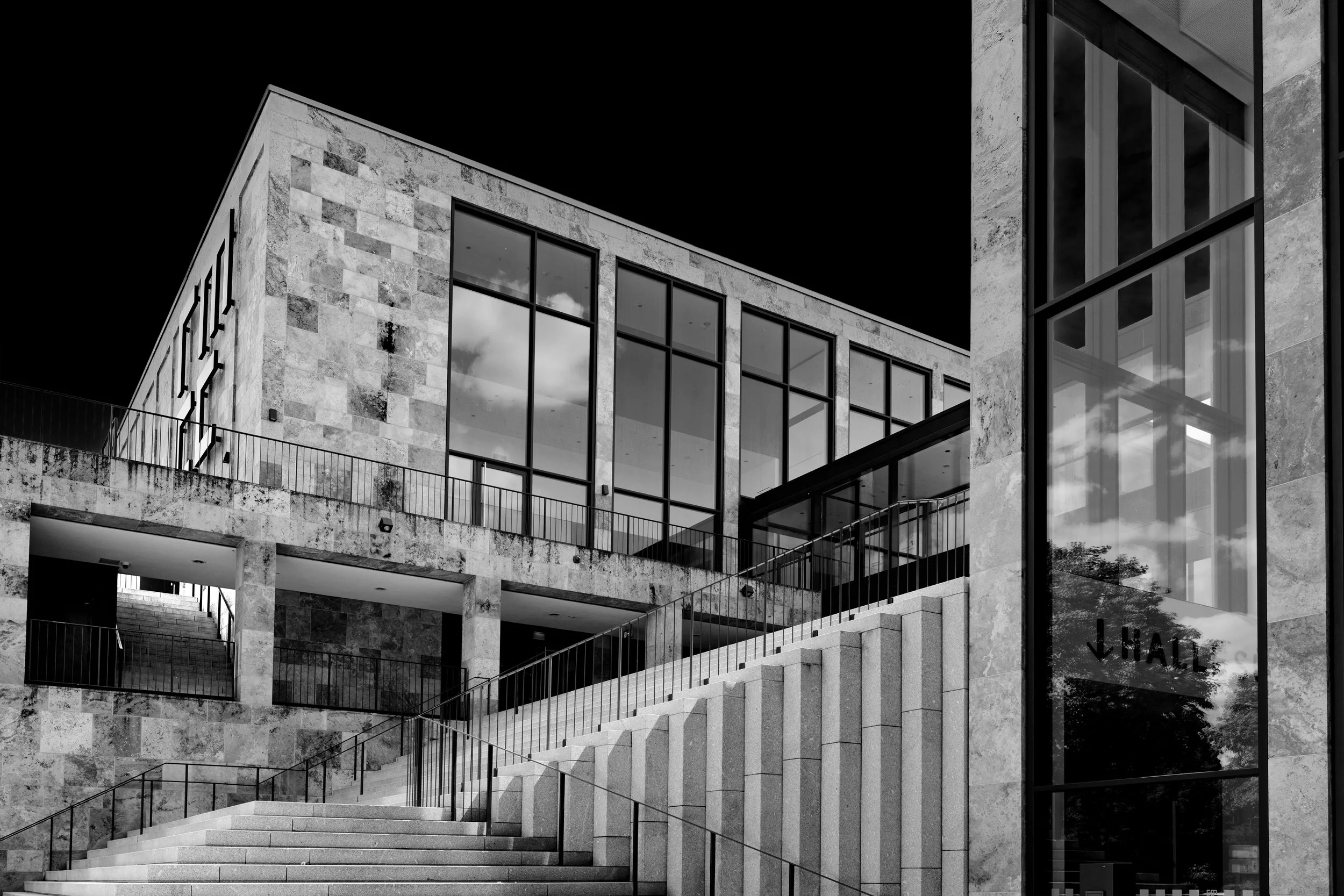 Modern multi-story building with large glass windows and stone exterior, featuring stairs and outdoor railings.