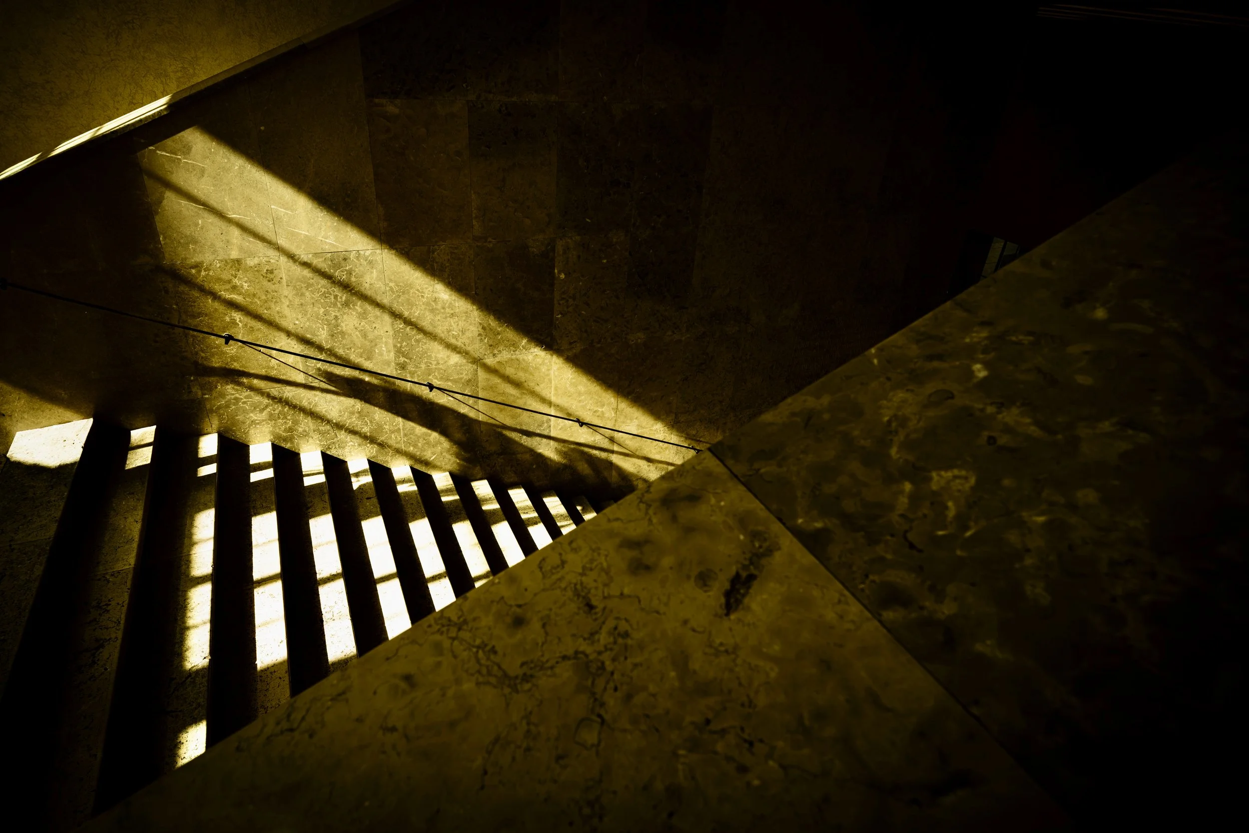 Looking down a staircase with shadows and sunlight cast on the marble walls and steps.