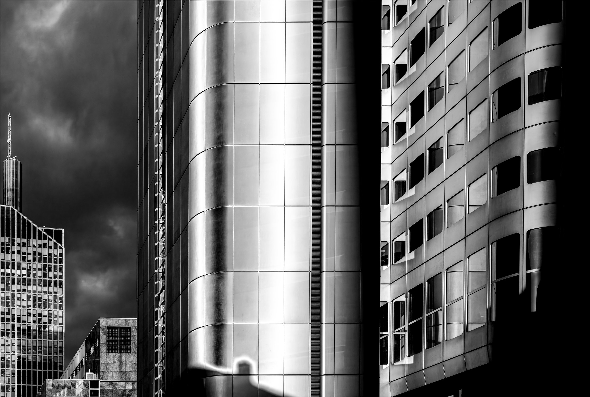 Black and white photo of modern high-rise buildings with reflective glass windows and a dark cloudy sky.