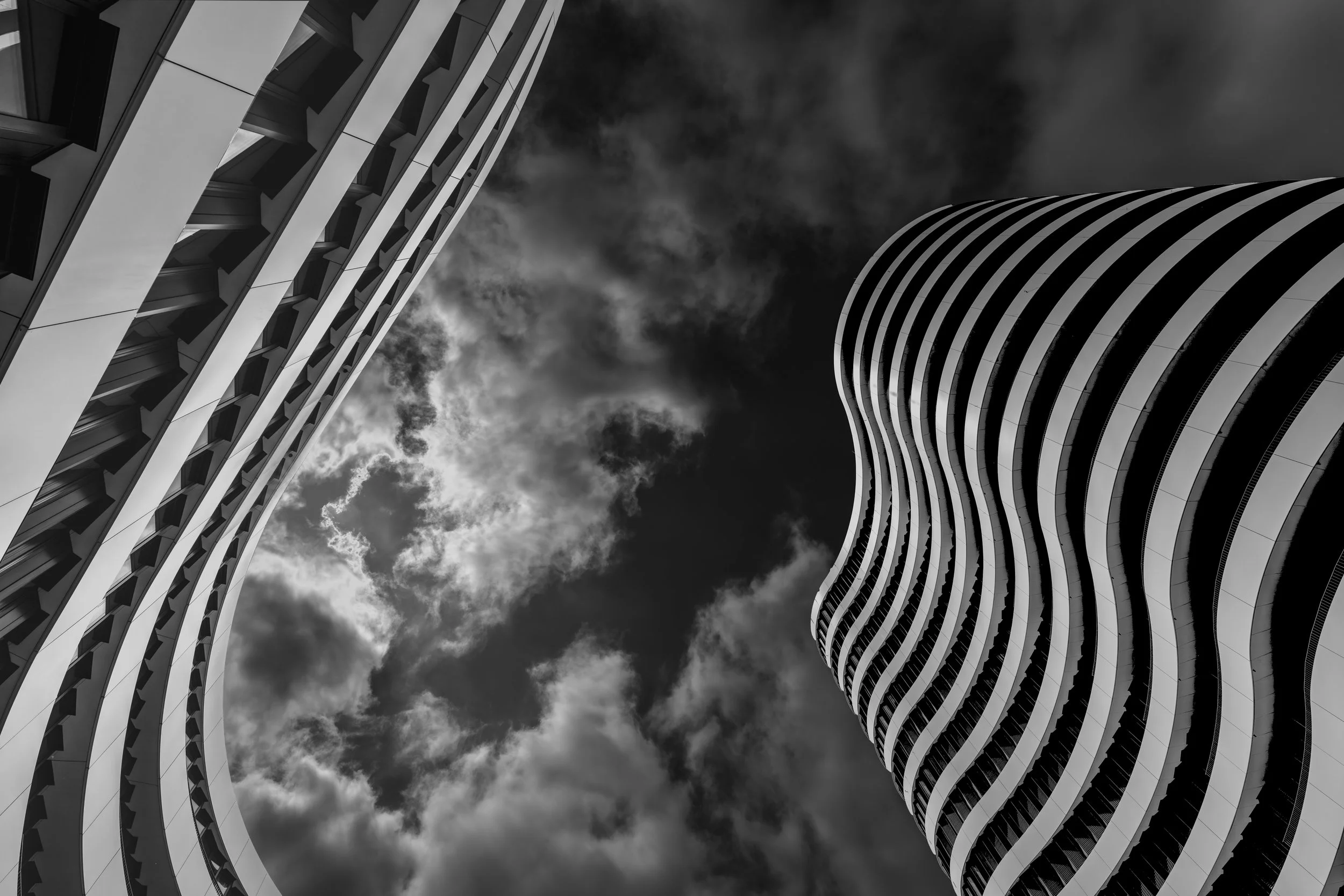 Looking up at two modern, curving high-rise buildings against a cloudy sky.