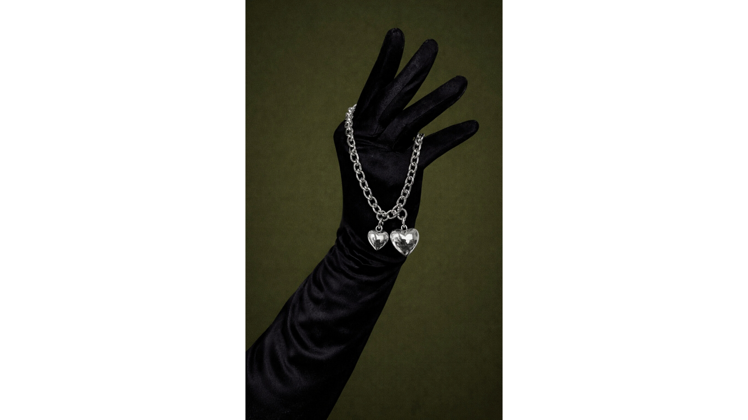 A hand wearing a black glove displaying a silver chain with two heart-shaped pendants.