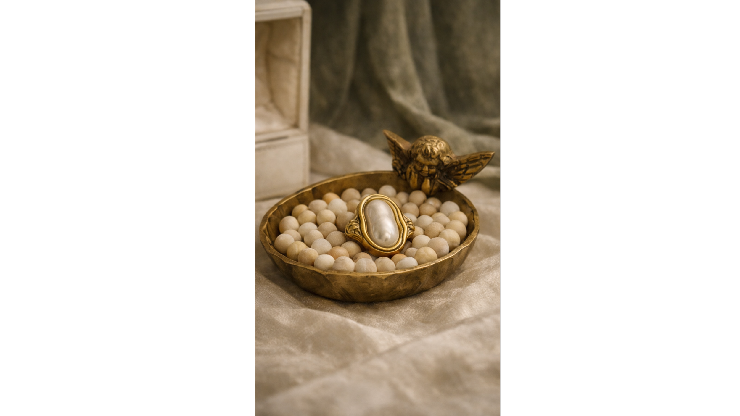 A gold bowl filled with small white round beads, a decorative gold and pearl picture frame, and a gold winged cherub figurine on a taupe satin cloth.