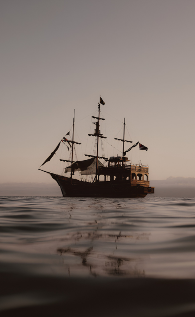 A historic sailing ship with multiple masts and flags floating on calm water during sunset or sunrise.