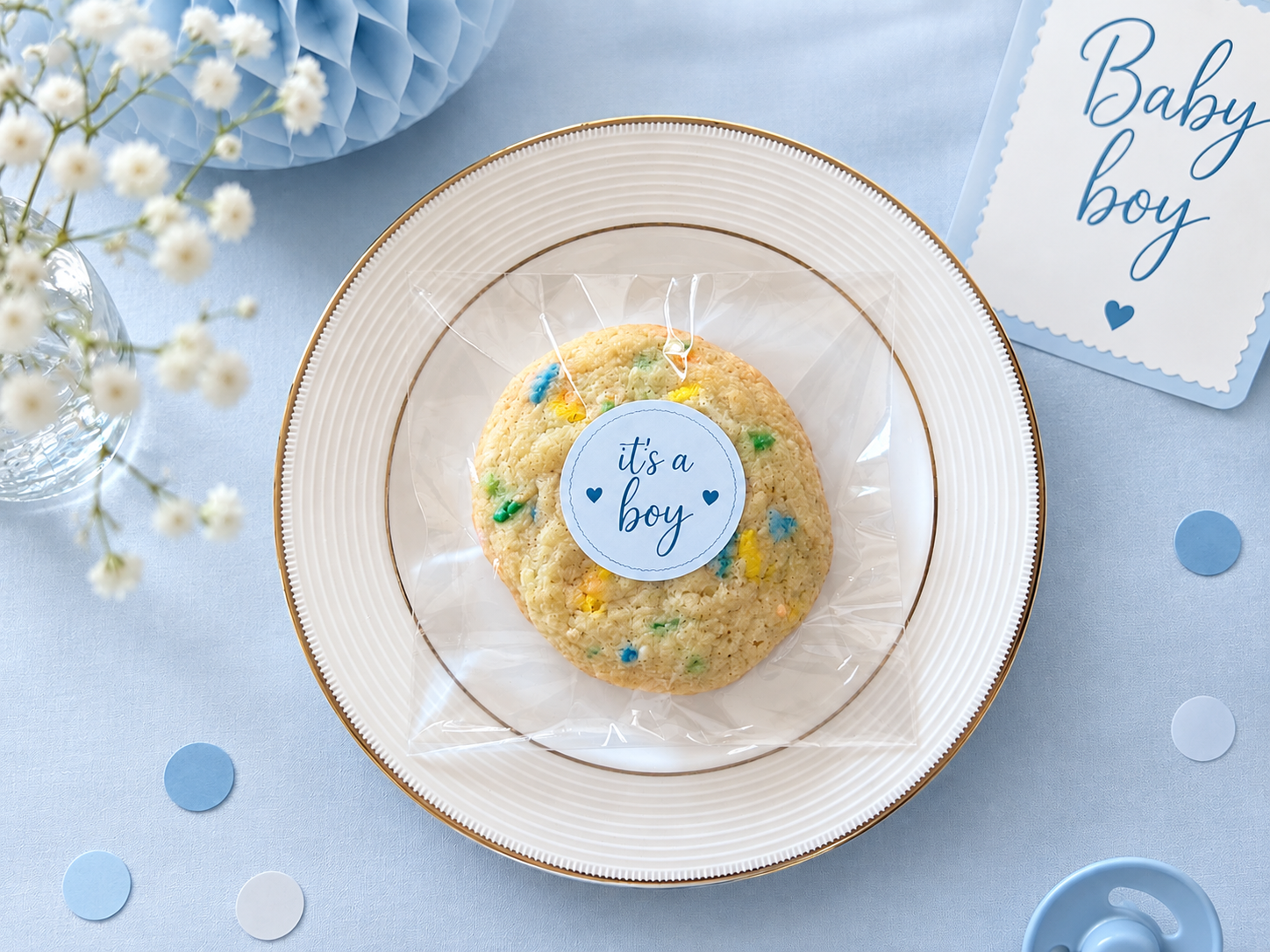 A table with a blue-themed baby boy celebration setup including a flower bouquet and a cookie bag tied with blue sticker.