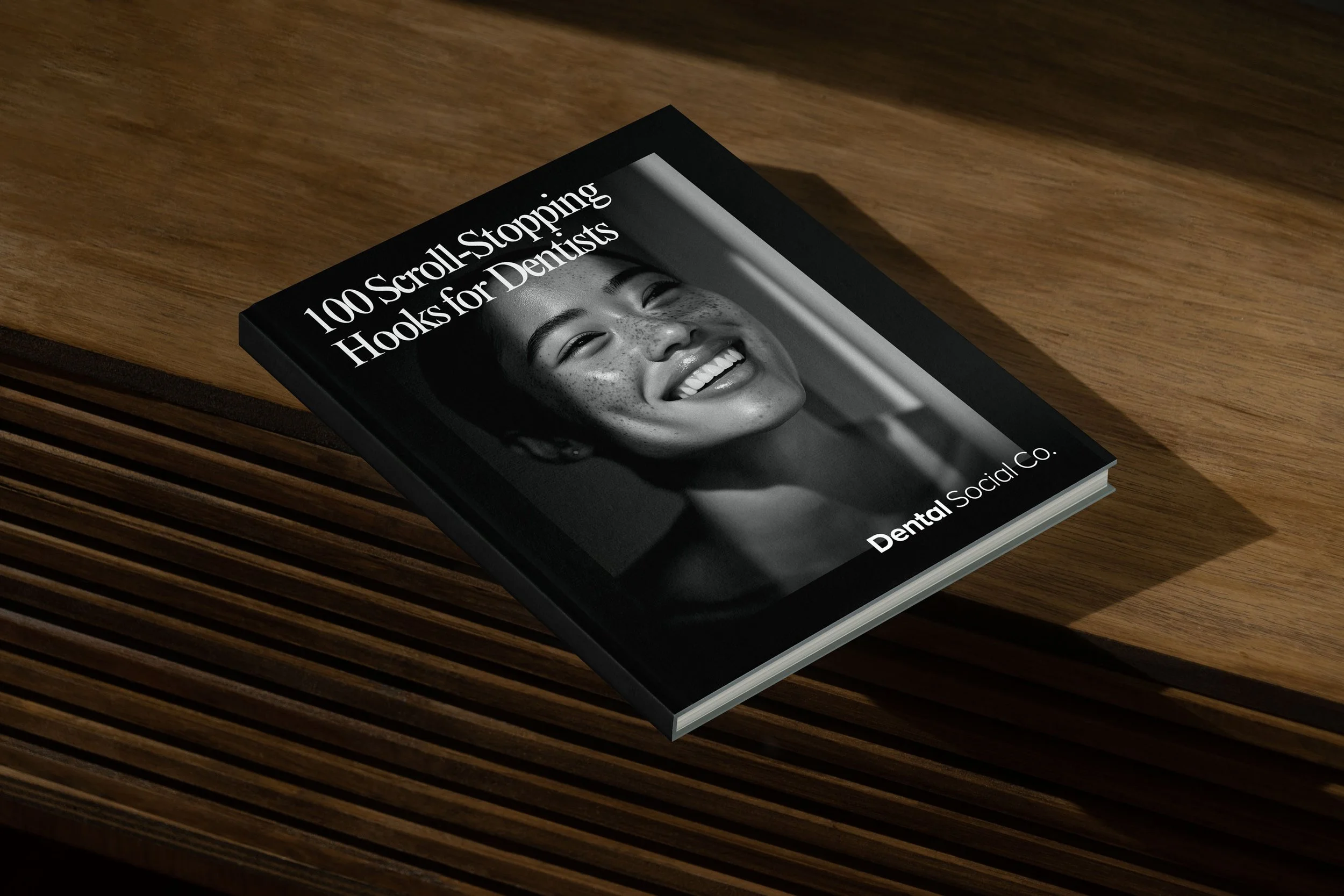 Brochure or magazine titled '100 Scroll-Stopping Hooks for Dentists,' featuring a smiling woman with dark hair and freckles, in grayscale, on a wooden surface.