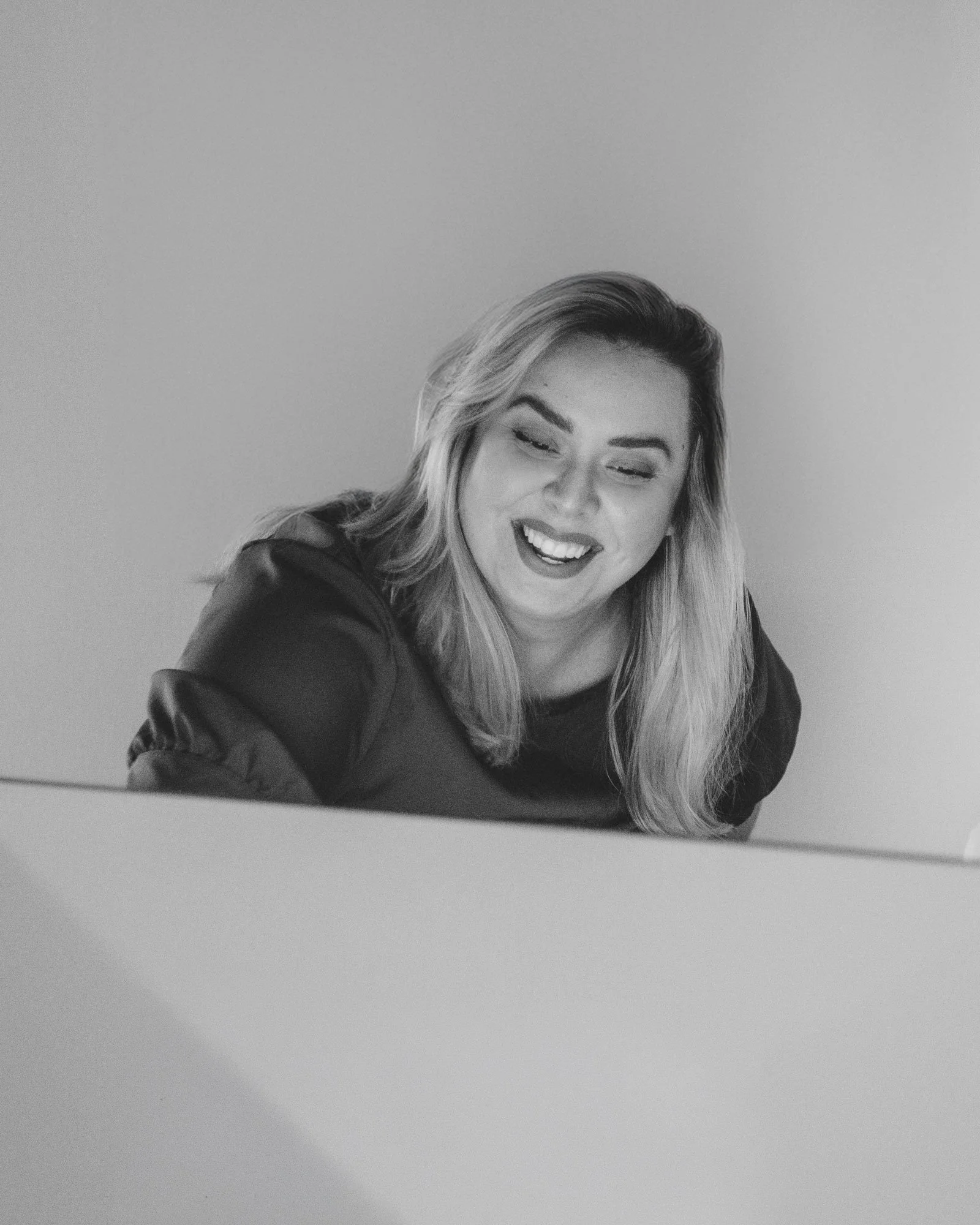 Black and white photo of a woman with long hair, smiling with eyes closed, against a plain background.