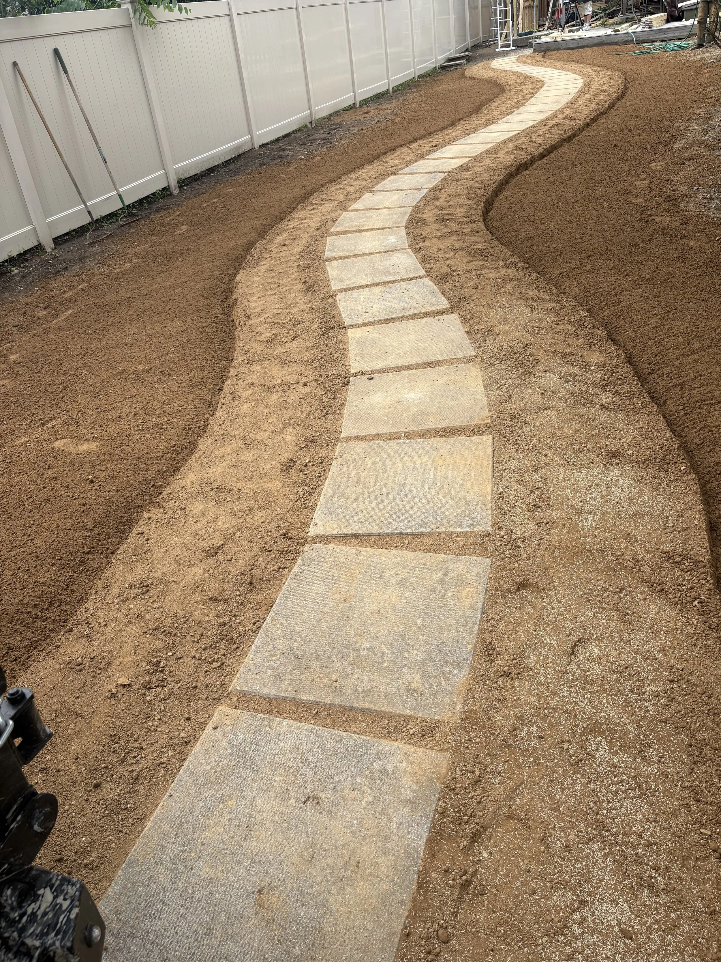 Curved stone pathway under construction in a backyard, with finished paving stones and nearby landscaping tools.