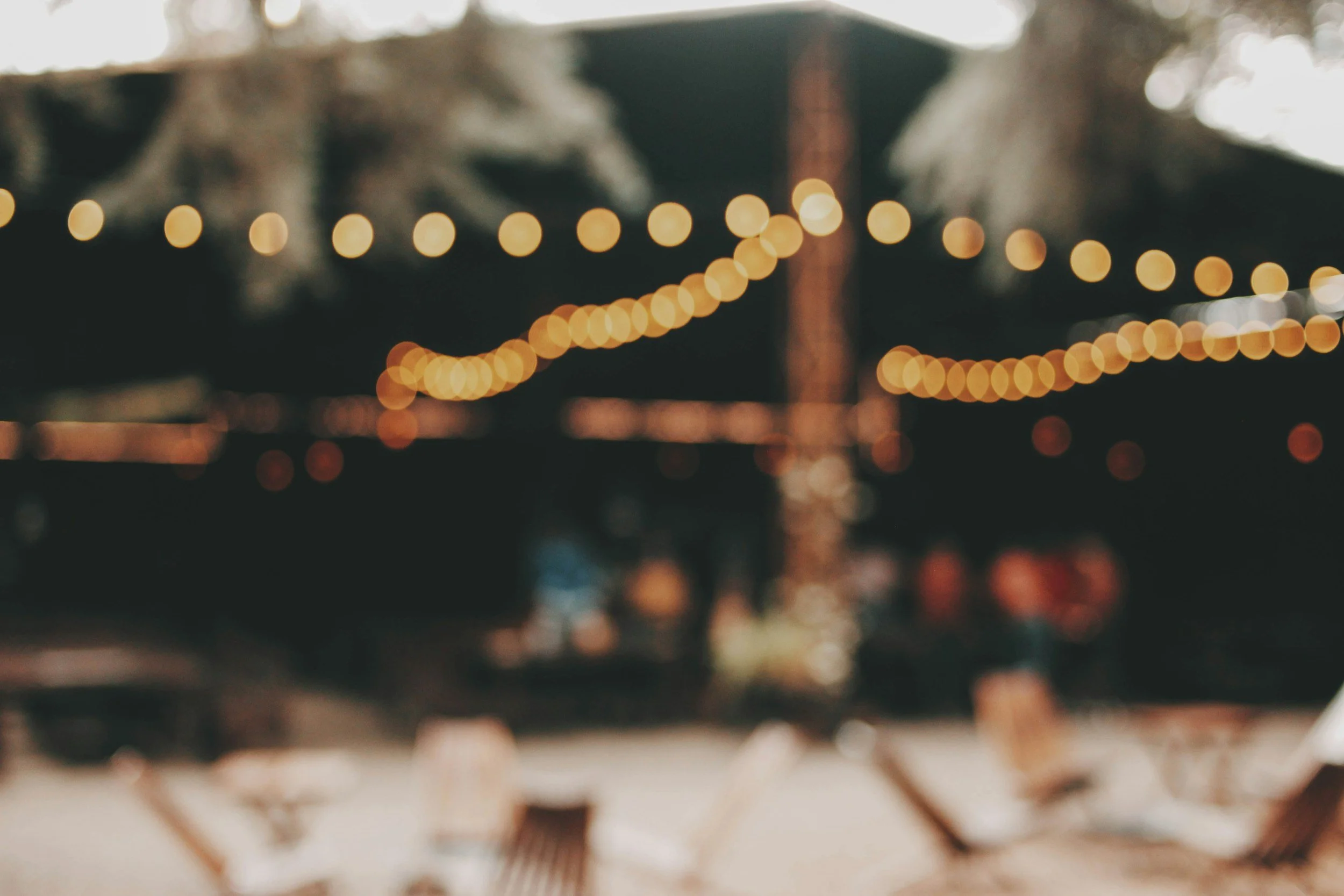 Blurred view of string lights hanging in an outdoor area at night.