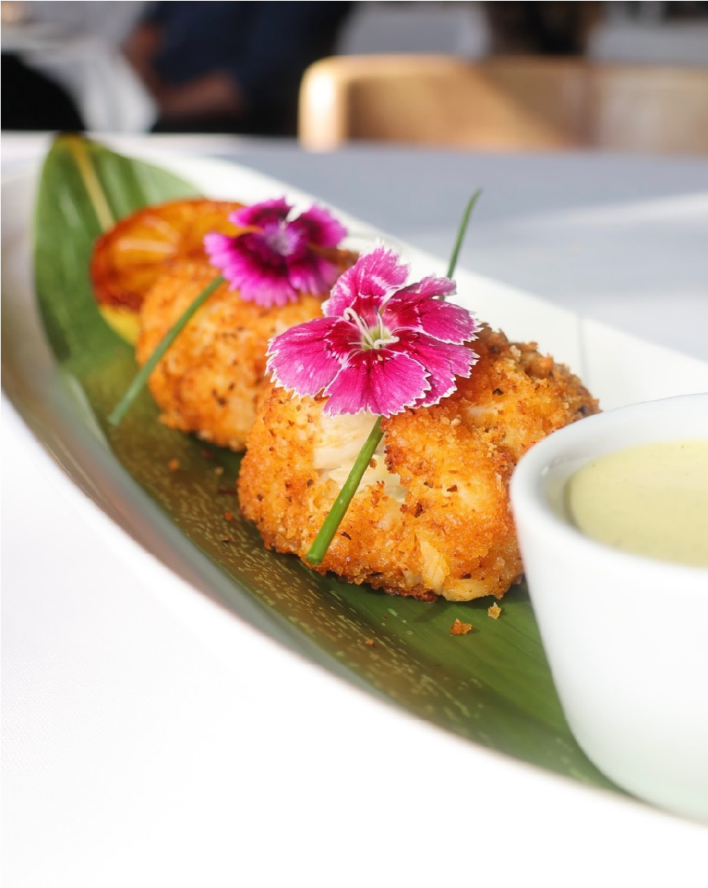 Fried seafood dish garnished with pink flowers and served with dipping sauce on a banana leaf