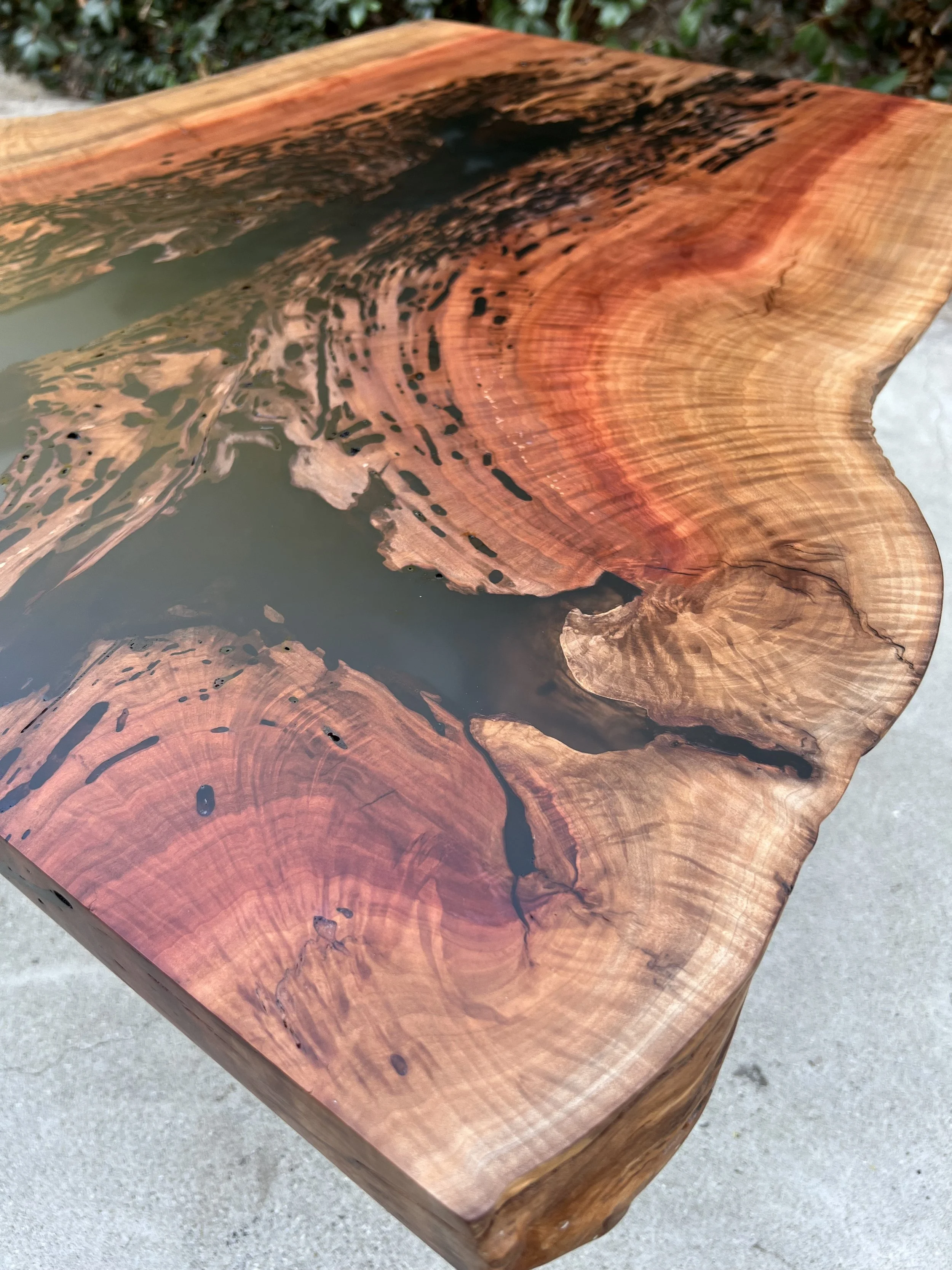 Close-up of a polished wooden table with natural wood grain and black resin details.