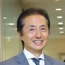 Smiling Asian man in a suit and tie in an indoor office setting.