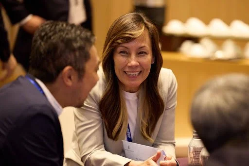 A woman with long brown hair smiling and talking to a man with short brown hair in a professional setting.