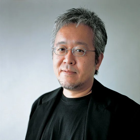 A middle-aged man with gray hair and glasses, wearing a black shirt and black blazer, smiling slightly against a plain gray background.