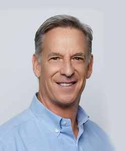A middle-aged man with gray hair wearing a light blue button-up shirt, smiling at the camera.