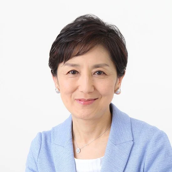 Portrait of a middle-aged woman with short dark hair, wearing a light blue blazer and a necklace, smiling at the camera against a plain white background.