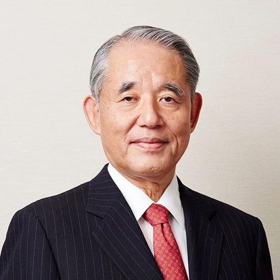 A professional elderly Asian man wearing a dark pinstripe suit, white shirt, and red tie, posing against a plain light-colored background.