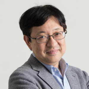 A man with glasses, black hair, wearing a light blue shirt and a gray blazer, smiling with arms crossed.