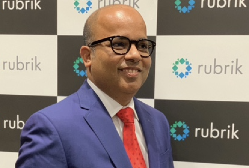 Man in blue suit and red tie smiling at a Rubrik event.