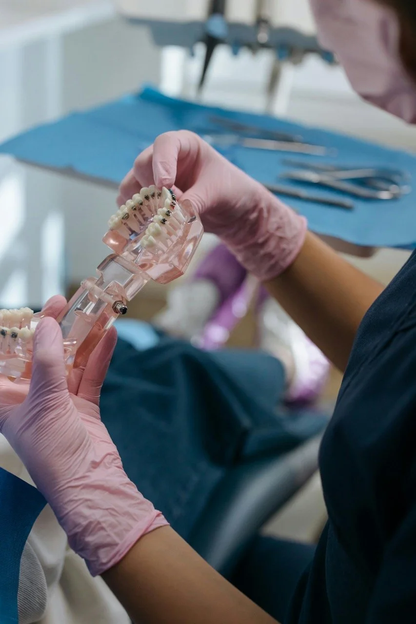 A dental technician handling a dental model with braces, wearing pink gloves in a dental laboratory setting.