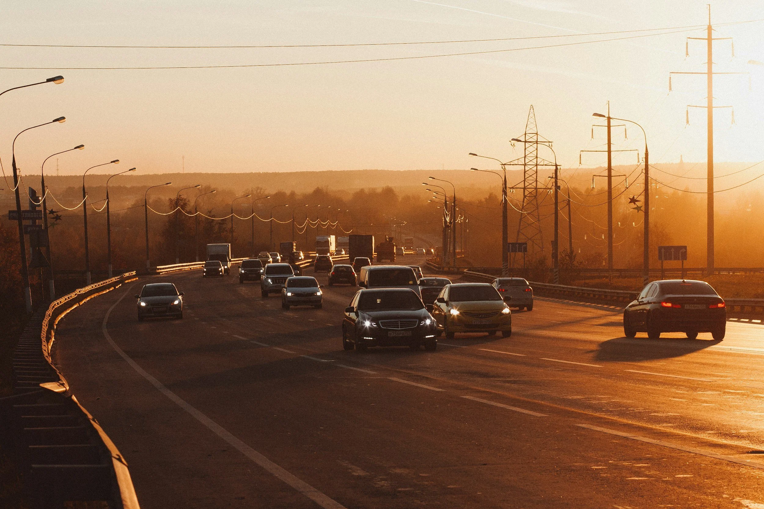 A highway with multiple cars driving during sunset, with streetlights and power lines along the road.