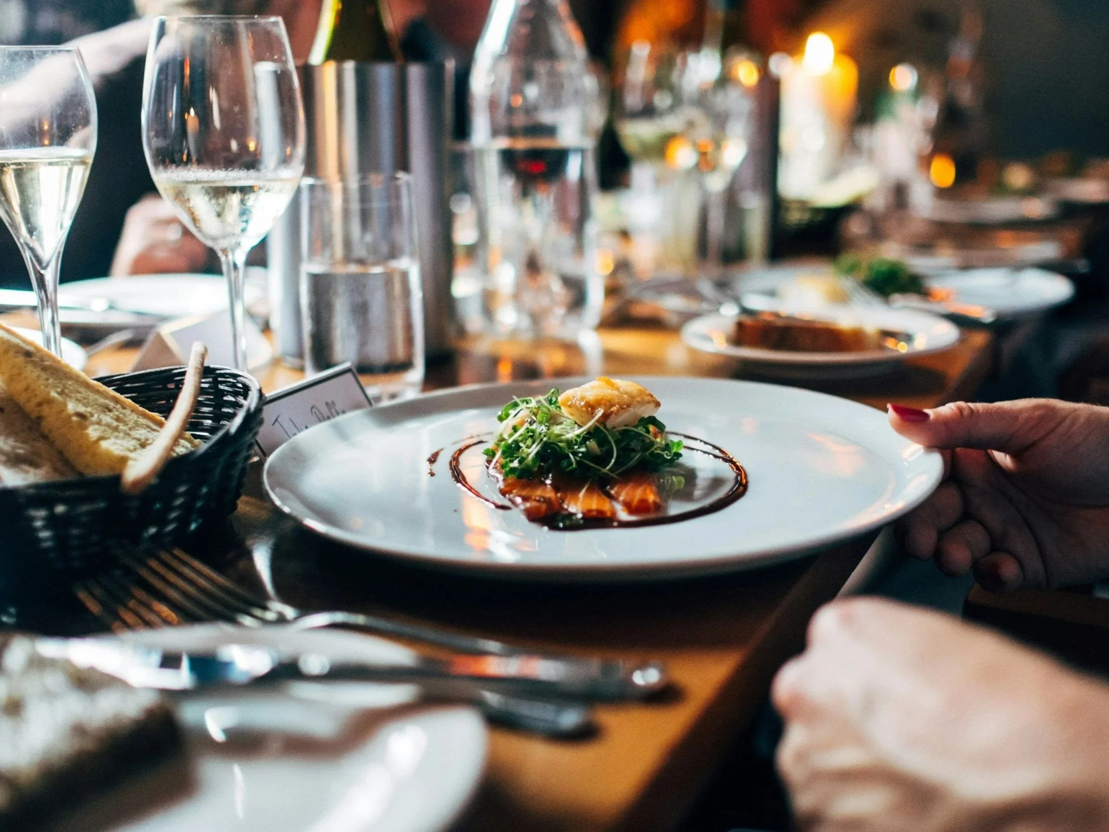 Close-up of a dinner table set with wine glasses, plates, and food, with people dining in the background.