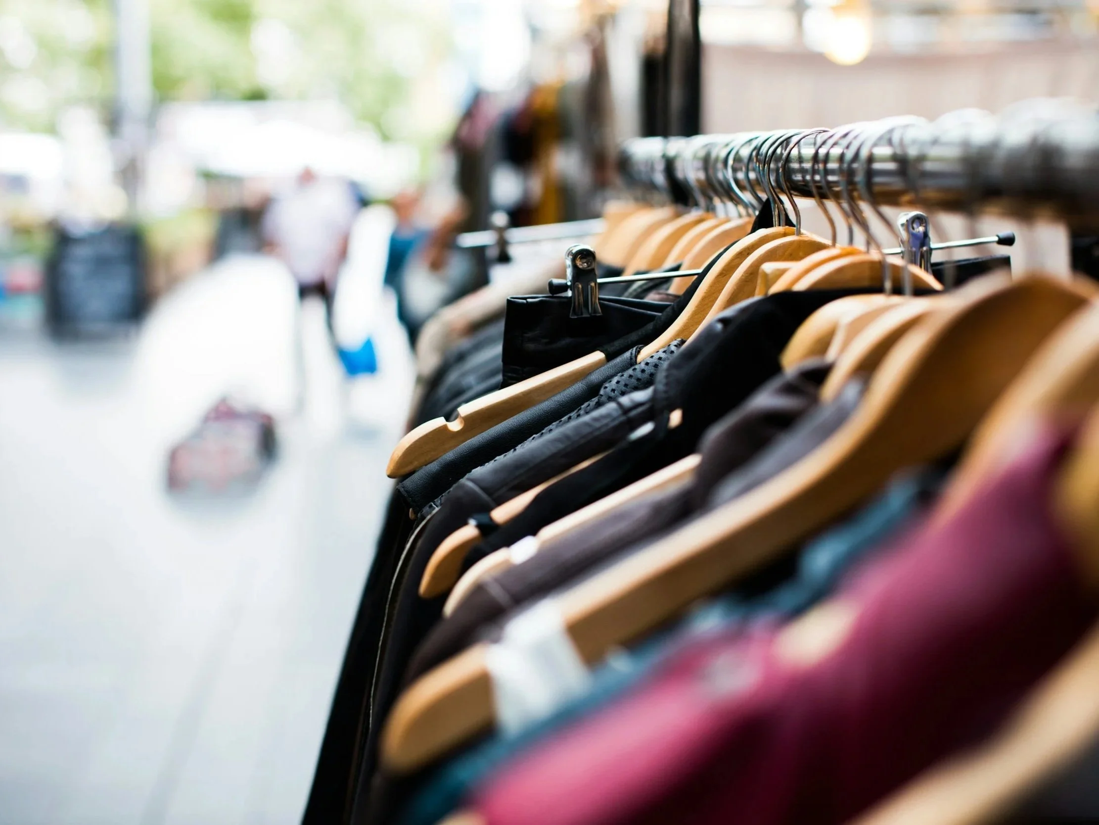 Clothing rack with various garments hanging on wooden hangers in a store.