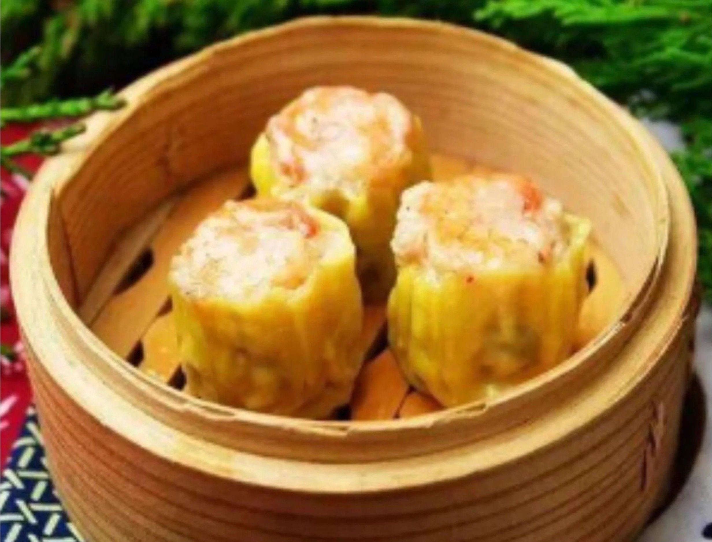 A bamboo steamer basket filled with yellow dumplings with a filling that appears to include shrimp or crab, resting on a colorful patterned cloth.